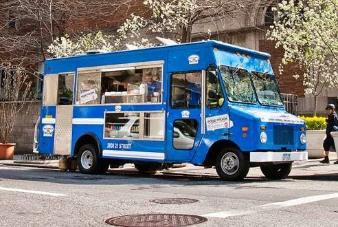 A blue food truck is parked on the side of the road.