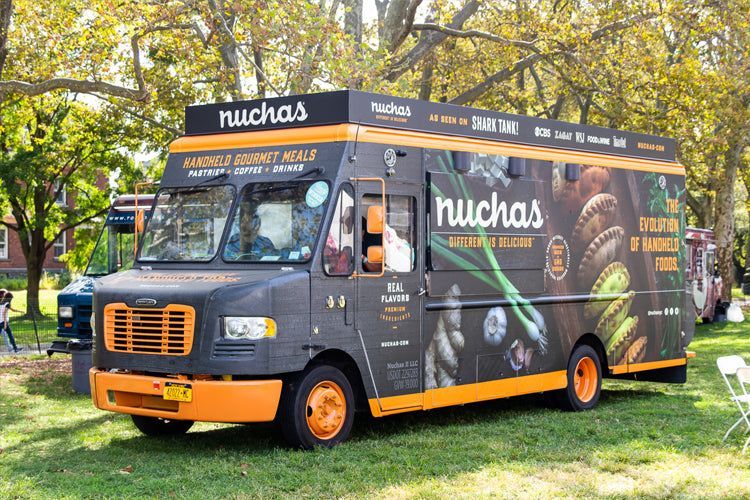 A black and orange food truck is parked in a grassy field.