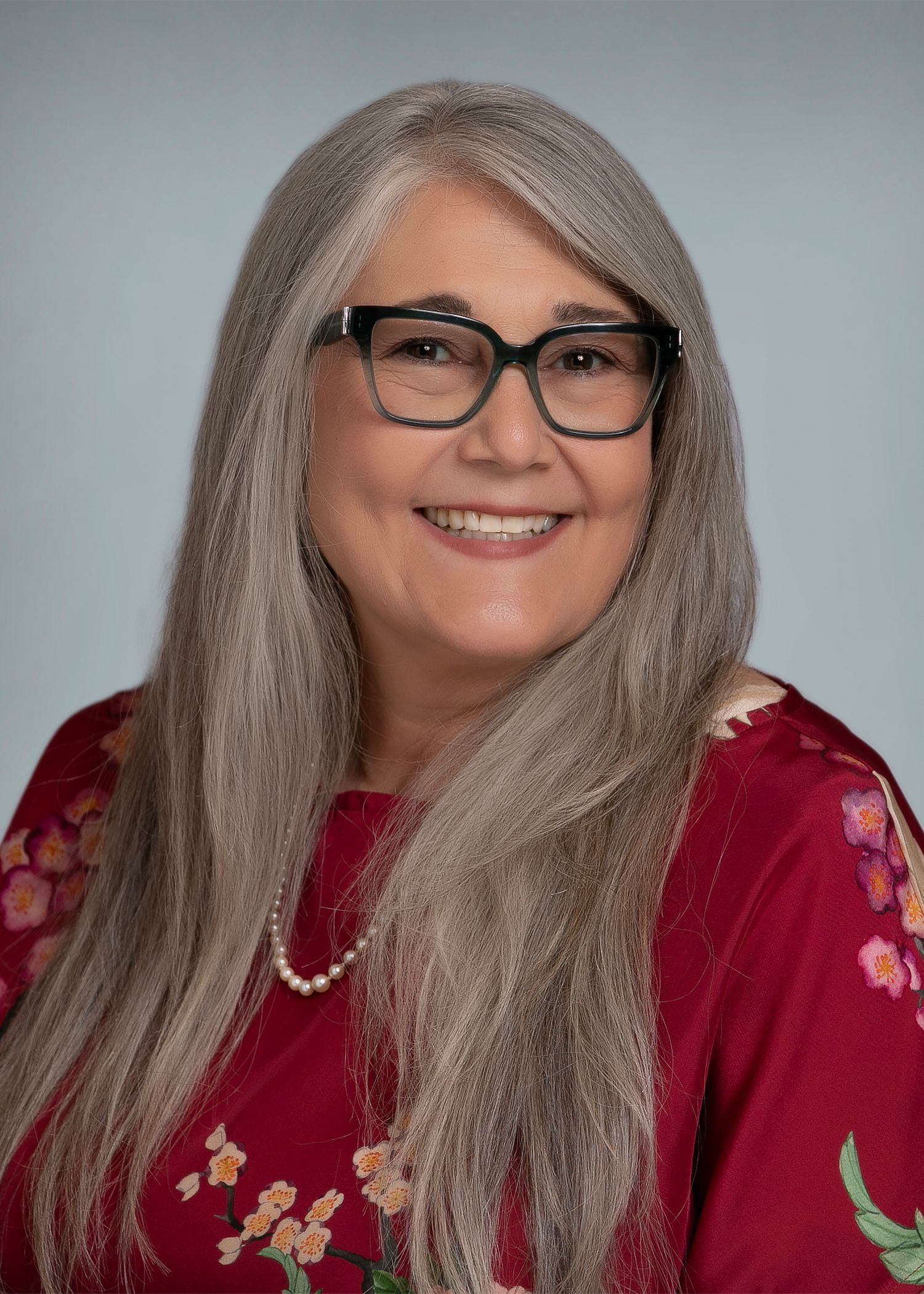 A woman wearing glasses and a red shirt is smiling for the camera.