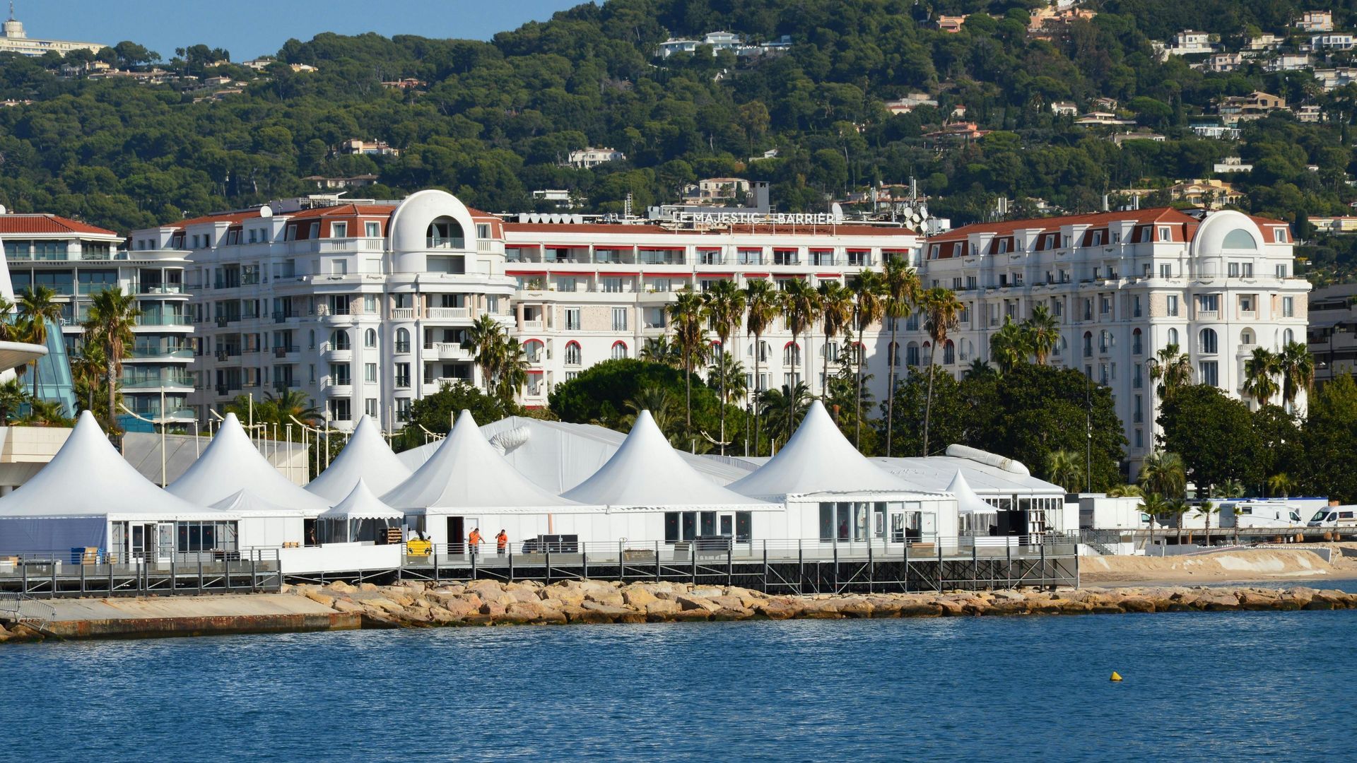 A row of white tents sit on the shore of a body of water