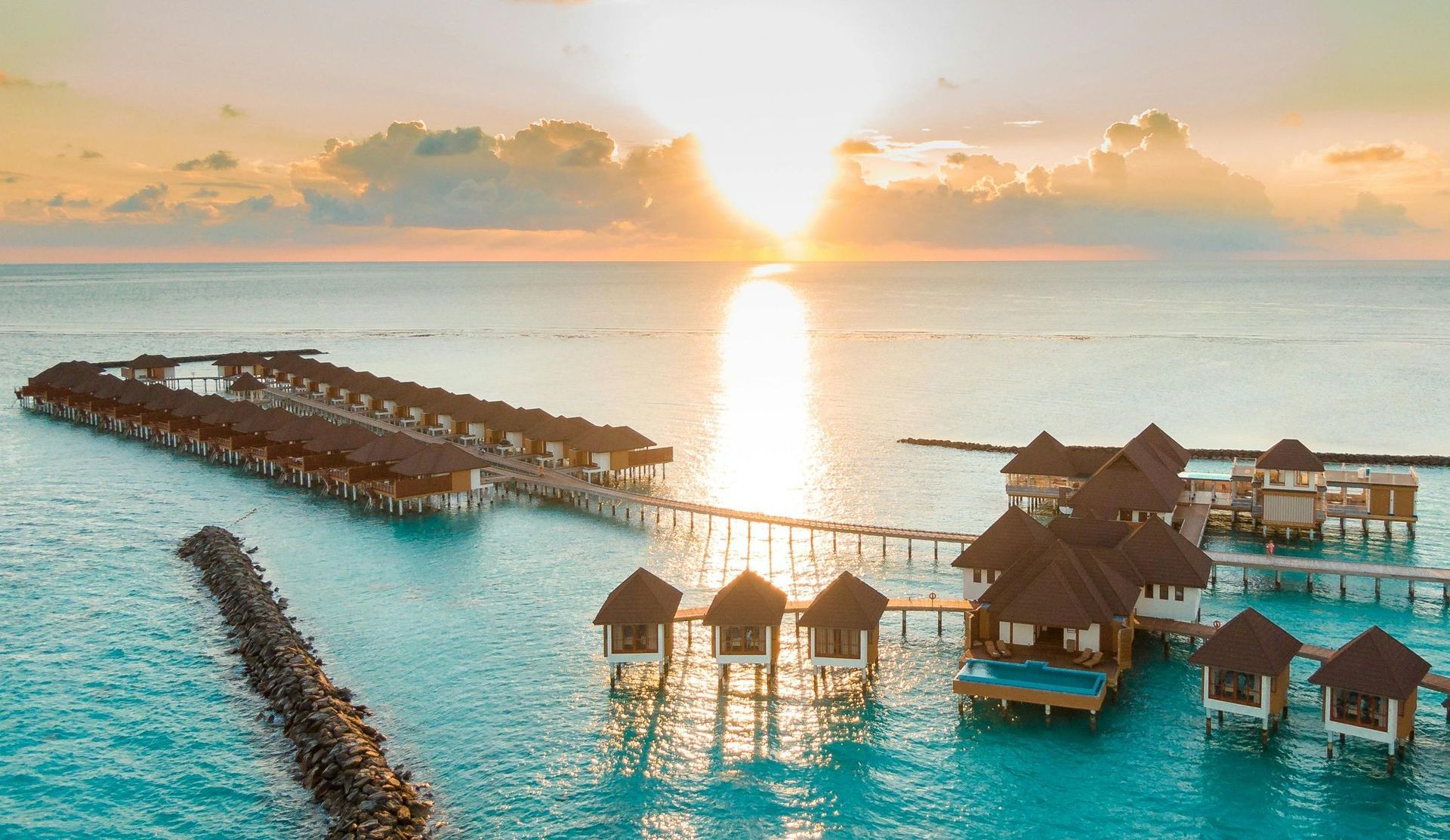 An aerial view of a resort in the middle of the ocean at sunset.