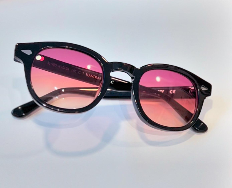 Occhiali da sole esposti su una rastrelliera metallica contro un muro di mattoni. Sono visibili modelli e colori assortiti.