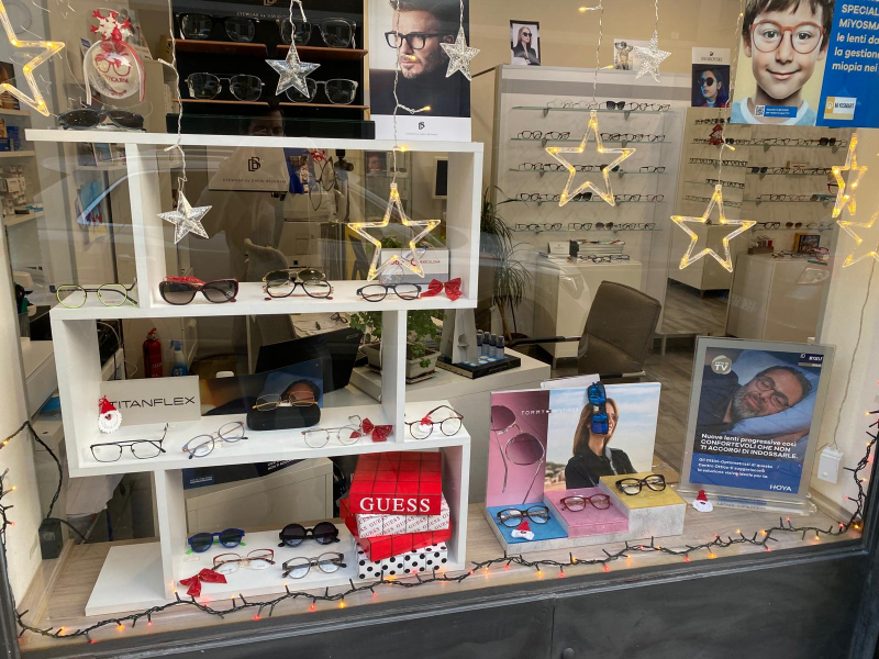 Occhiali da vista esposti, disposti su una parete bianca. Sono visibili montature di vari stili e colori.