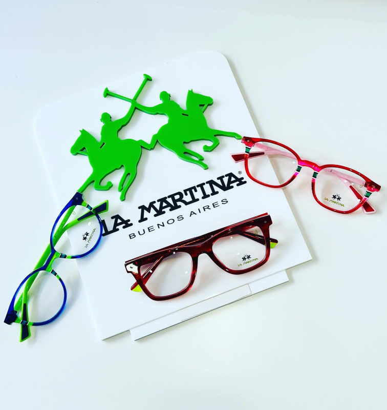 Primo piano di diversi occhiali esposti su una superficie bianca, tra cui un paio ben visibile con montatura blu.