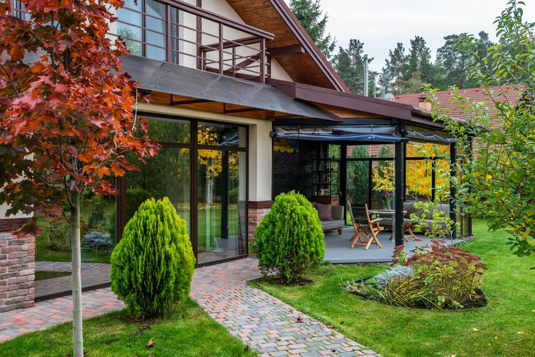 A large house with a large patio in front of it surrounded by trees and bushes.