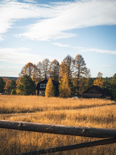 A wooden fence surrounds a field with a house in the background.