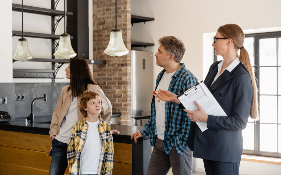People standing in a modern kitchen discussing the space with a realtor holding papers.
