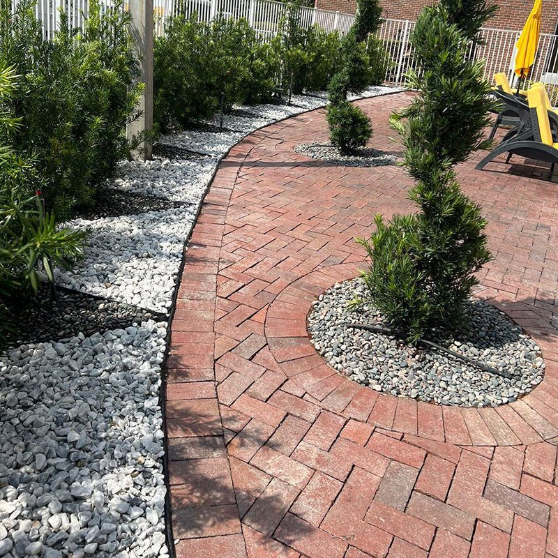 A brick walkway leading to a patio with trees and rocks.