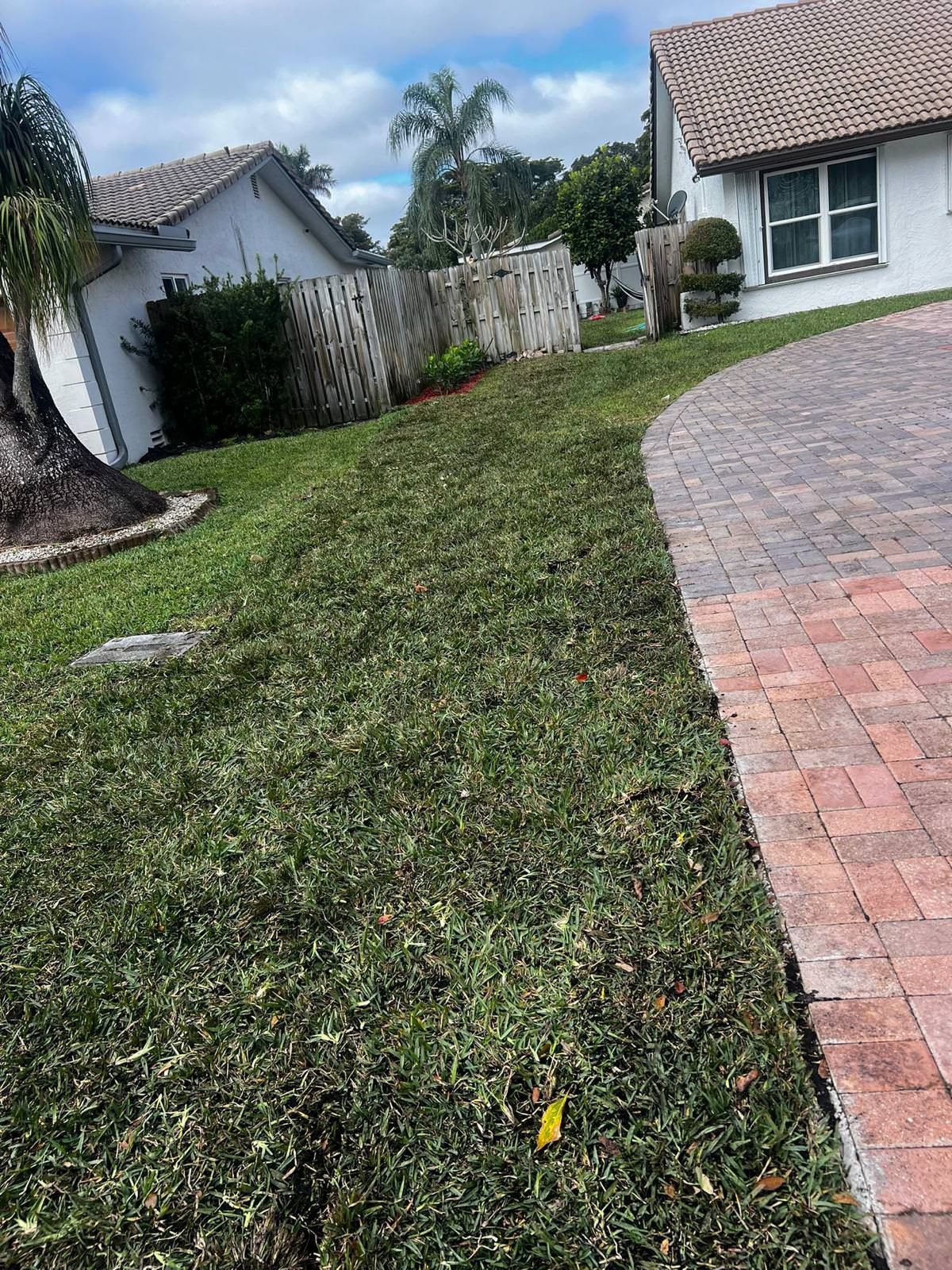 A brick driveway leading to a house with a lush green lawn.