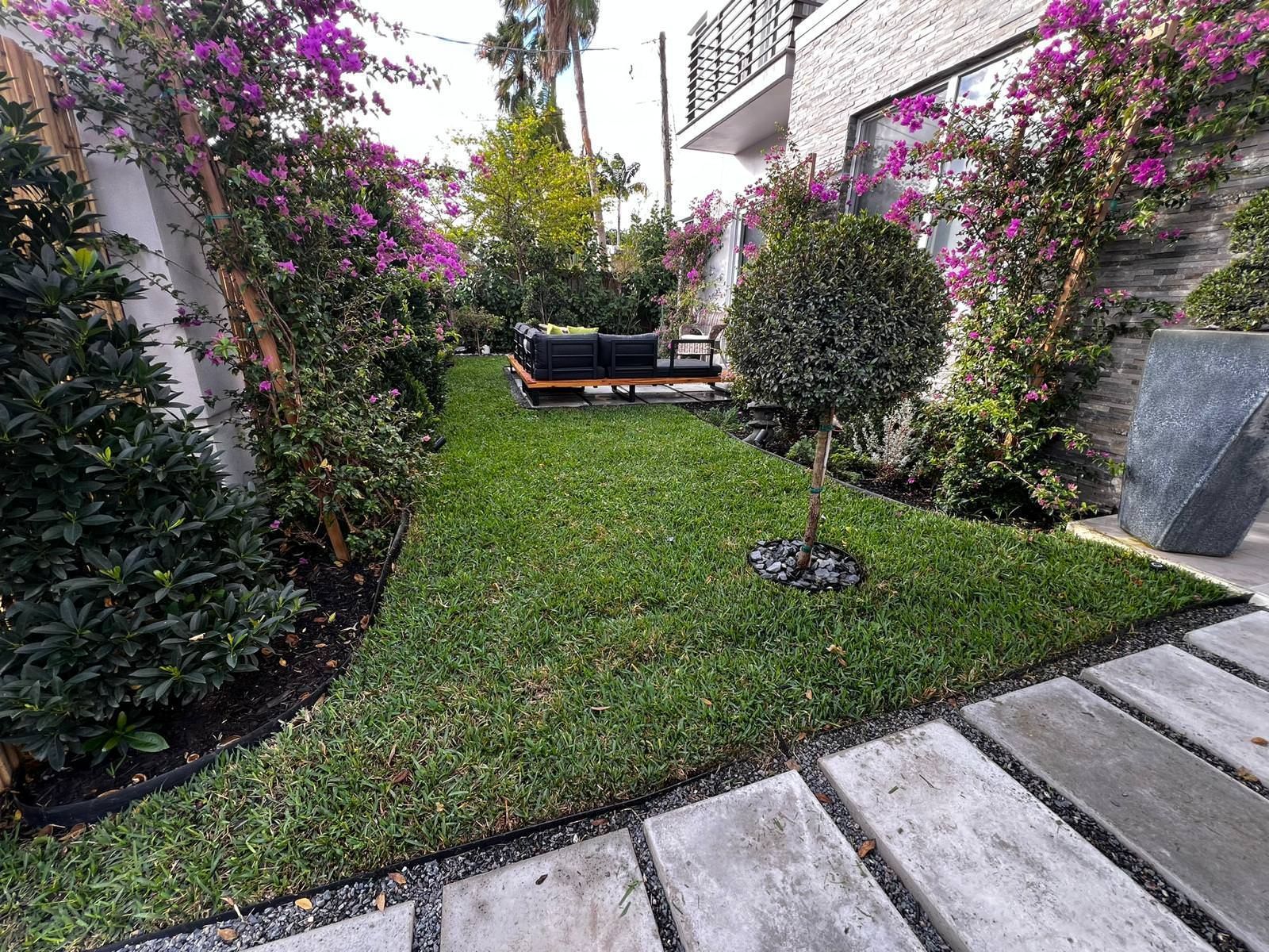 A lush green lawn with purple flowers and a concrete walkway.