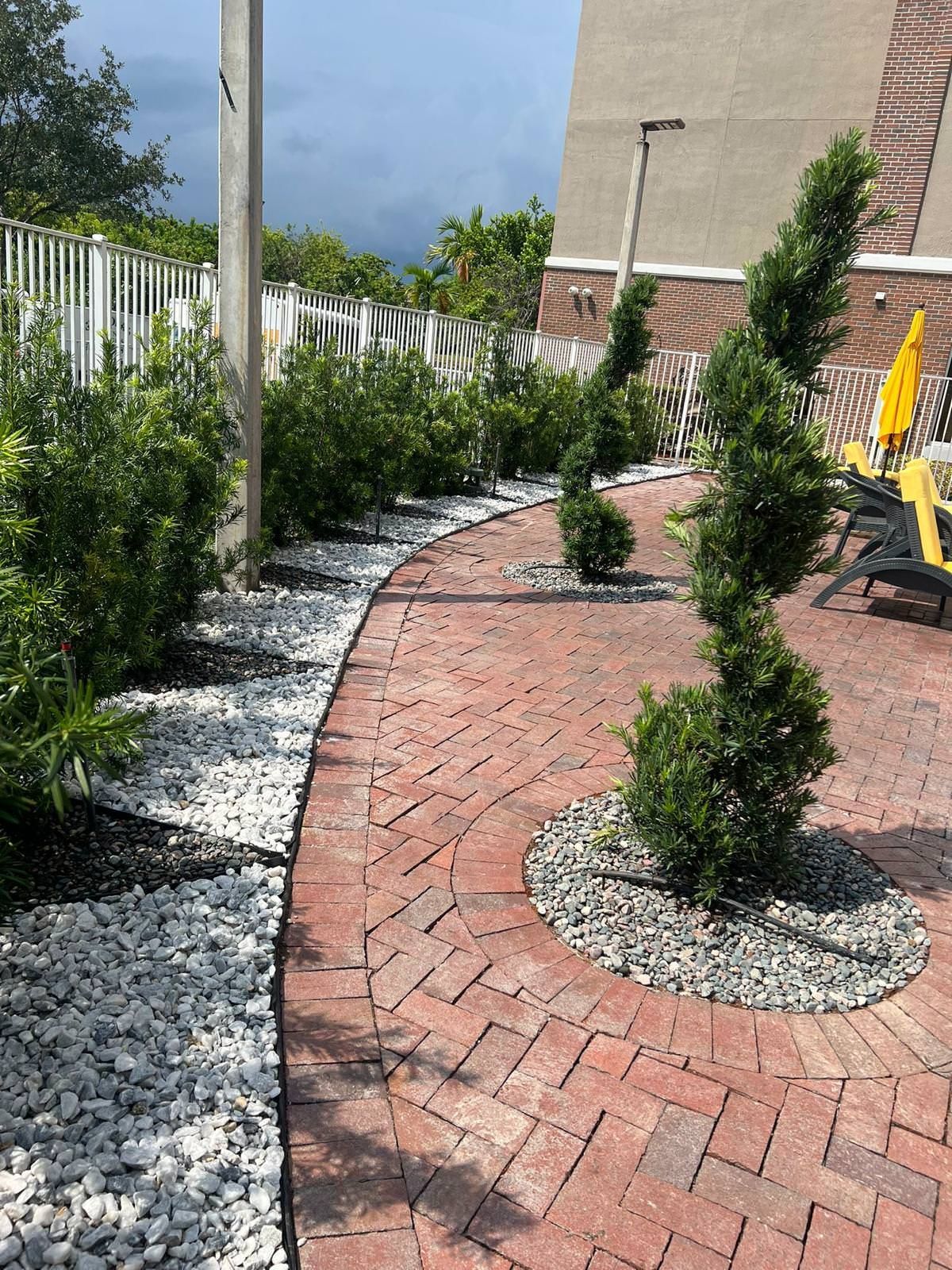A brick walkway surrounded by a patio with trees and rocks.