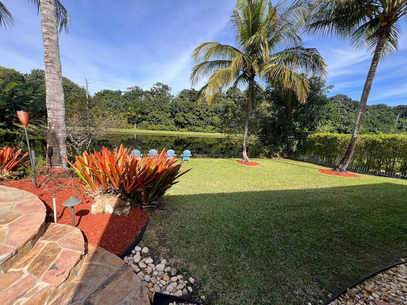 A lush green lawn with palm trees and a pond in the background.