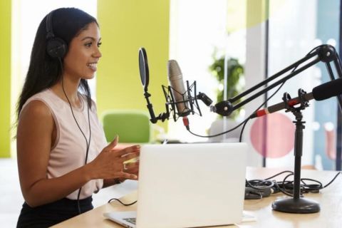 A woman is sitting at a desk with a laptop and a microphone.