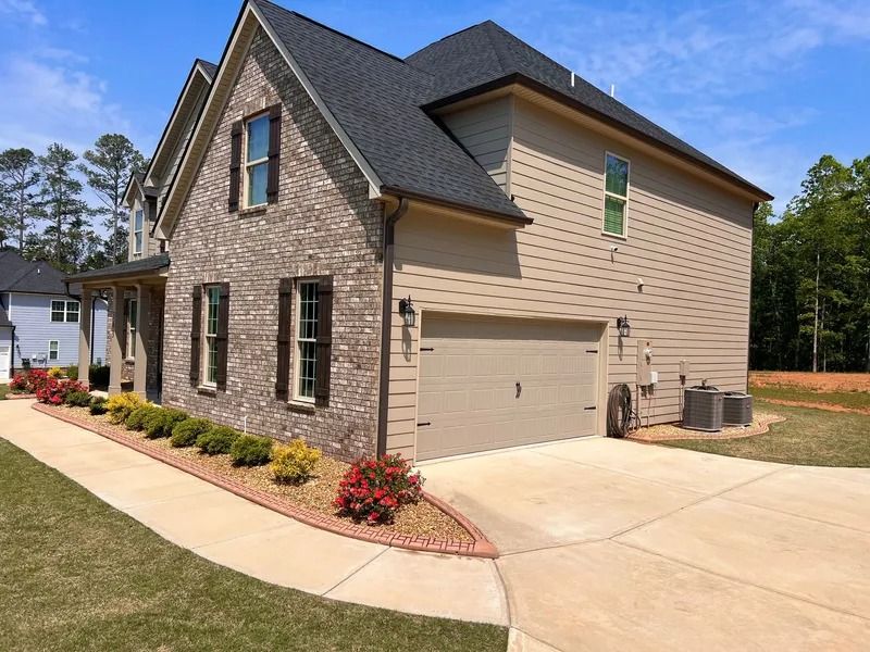Suburban two-story brick and siding house with attached garage, landscaped front yard, and driveway