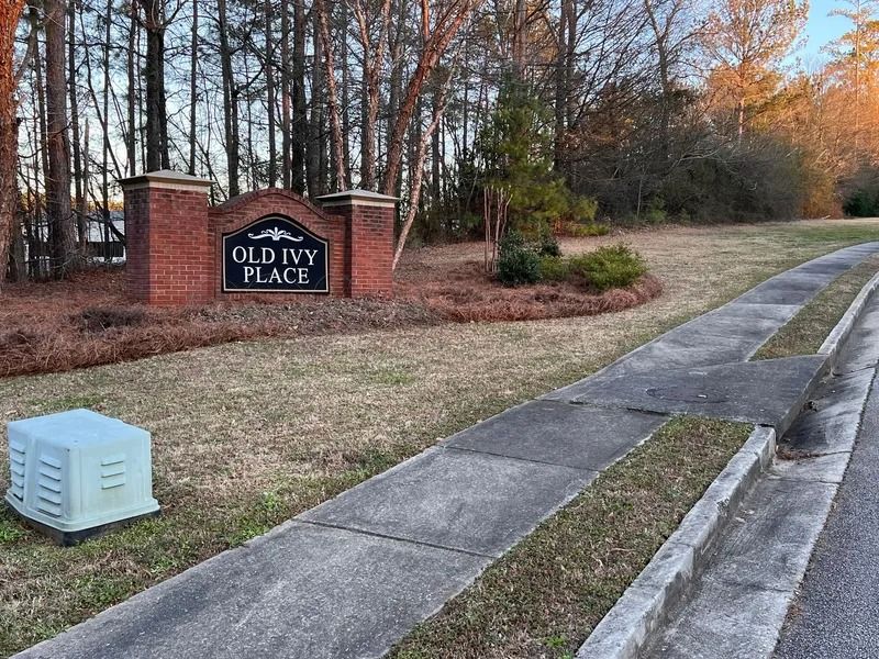 Brick entrance sign reading “Old Ivy Place” beside a sidewalk and trees in autumn.