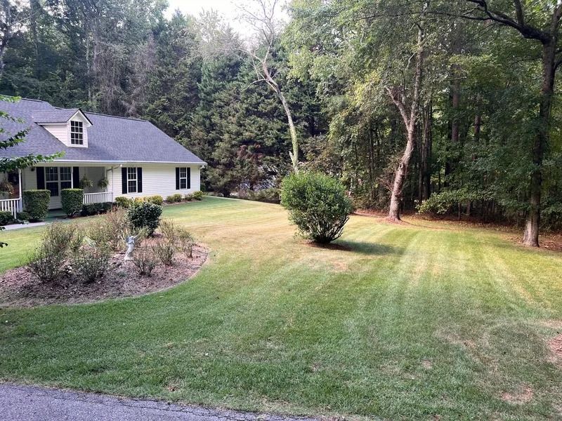 House with gray roof beside a wide green lawn and trees in a wooded yard