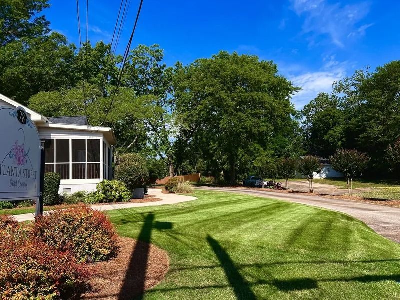 Lush front yard with trimmed lawn, flower beds, and a house under a bright blue sky