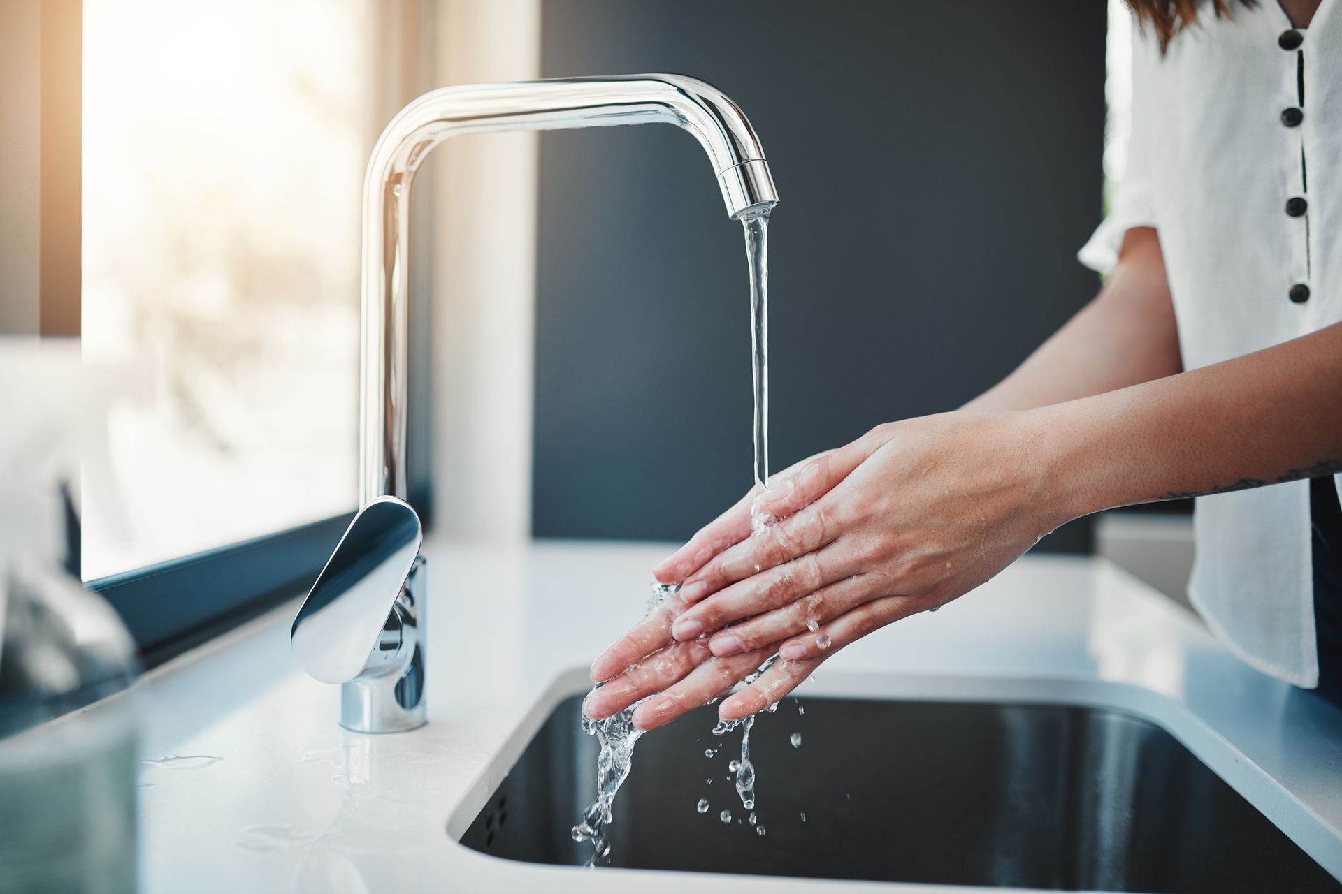 Person washing hands under a running faucet in a stainless steel sink.