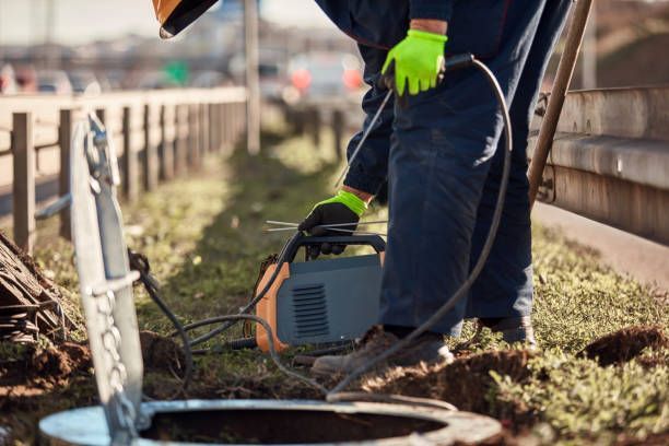 A worker in overalls welding near an open manhole, using welding equipment.