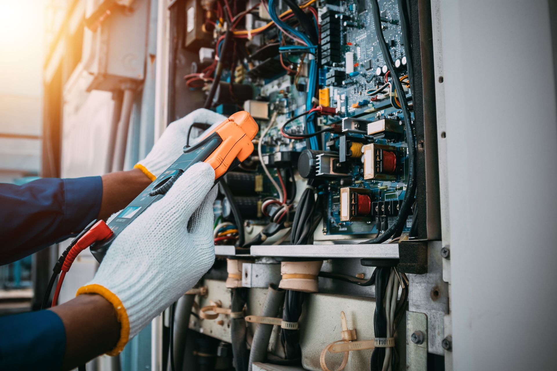 Hands in white gloves using a multimeter to inspect complex electrical wiring inside a cabinet.