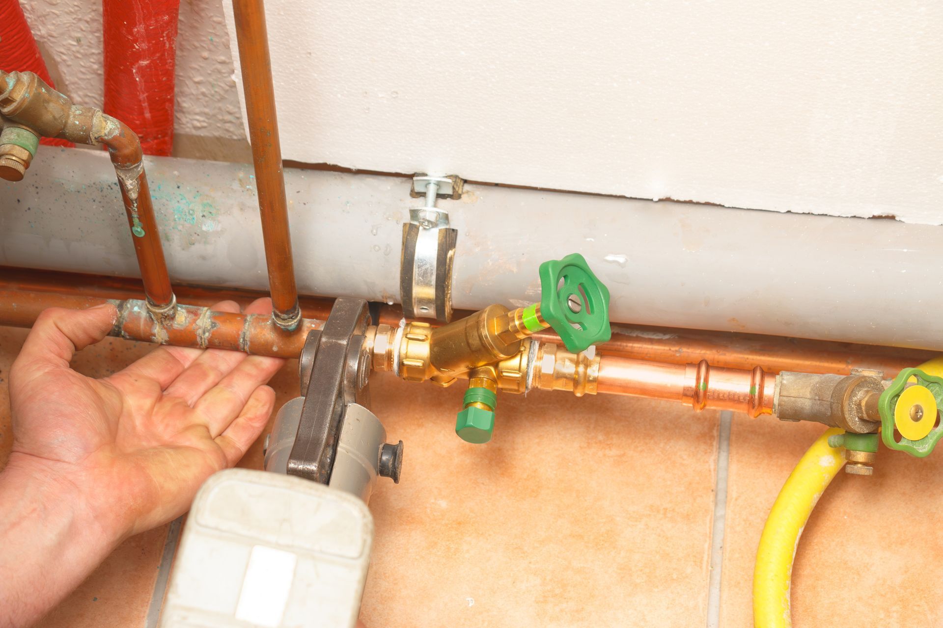 Hand using a wrench to tighten copper pipes and valves in a plumbing system.