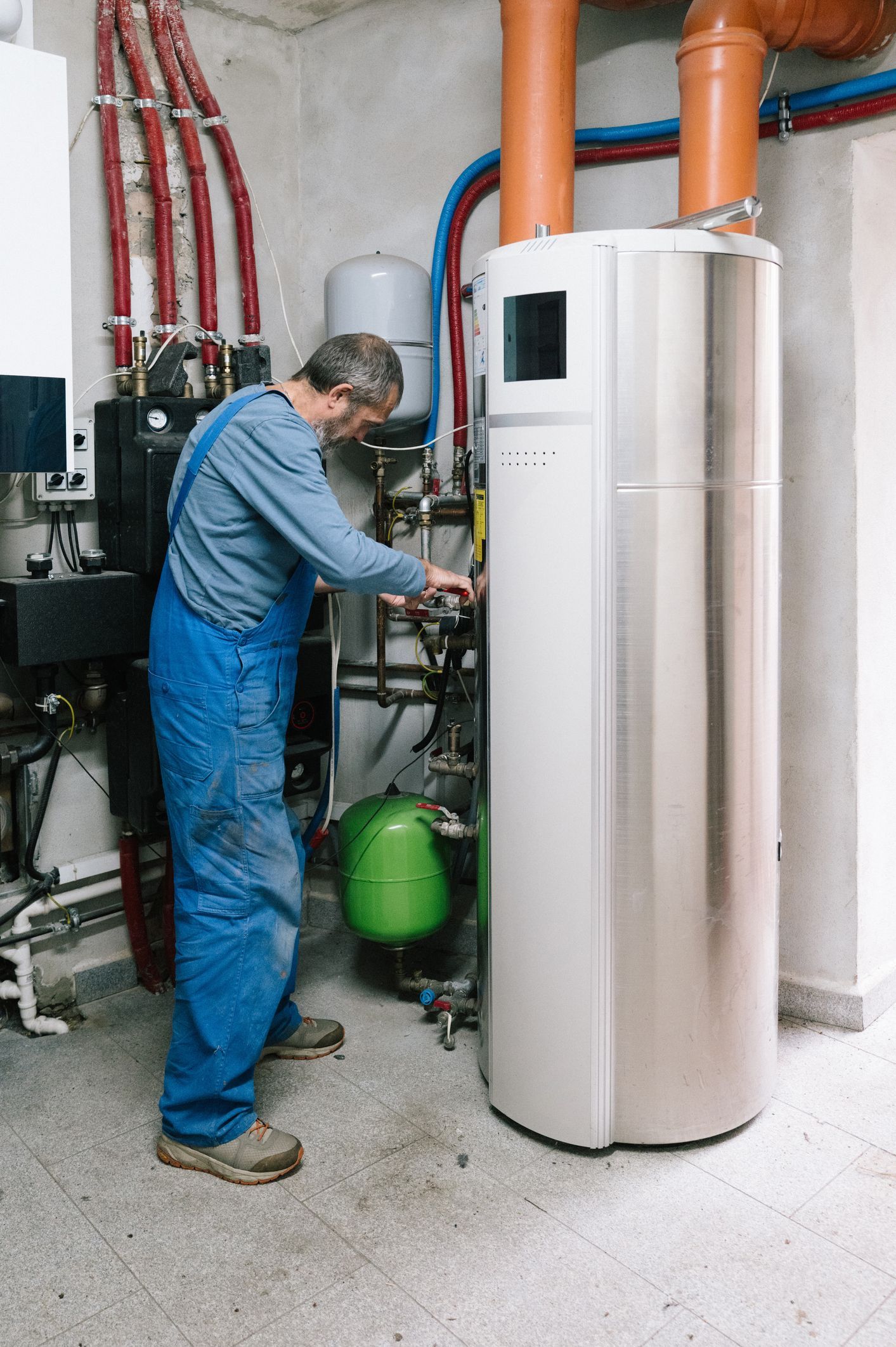 Hand holding remote, adjusting wall-mounted air conditioner displaying 21 degrees. White unit, white wall, interior.