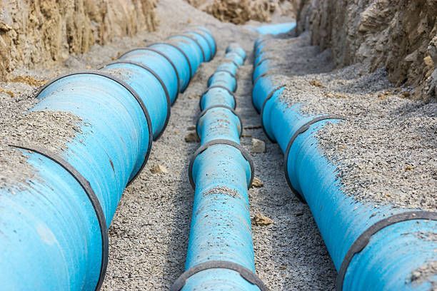 Blue water pipes laid in a trench, ready for covering, on a bed of gravel.