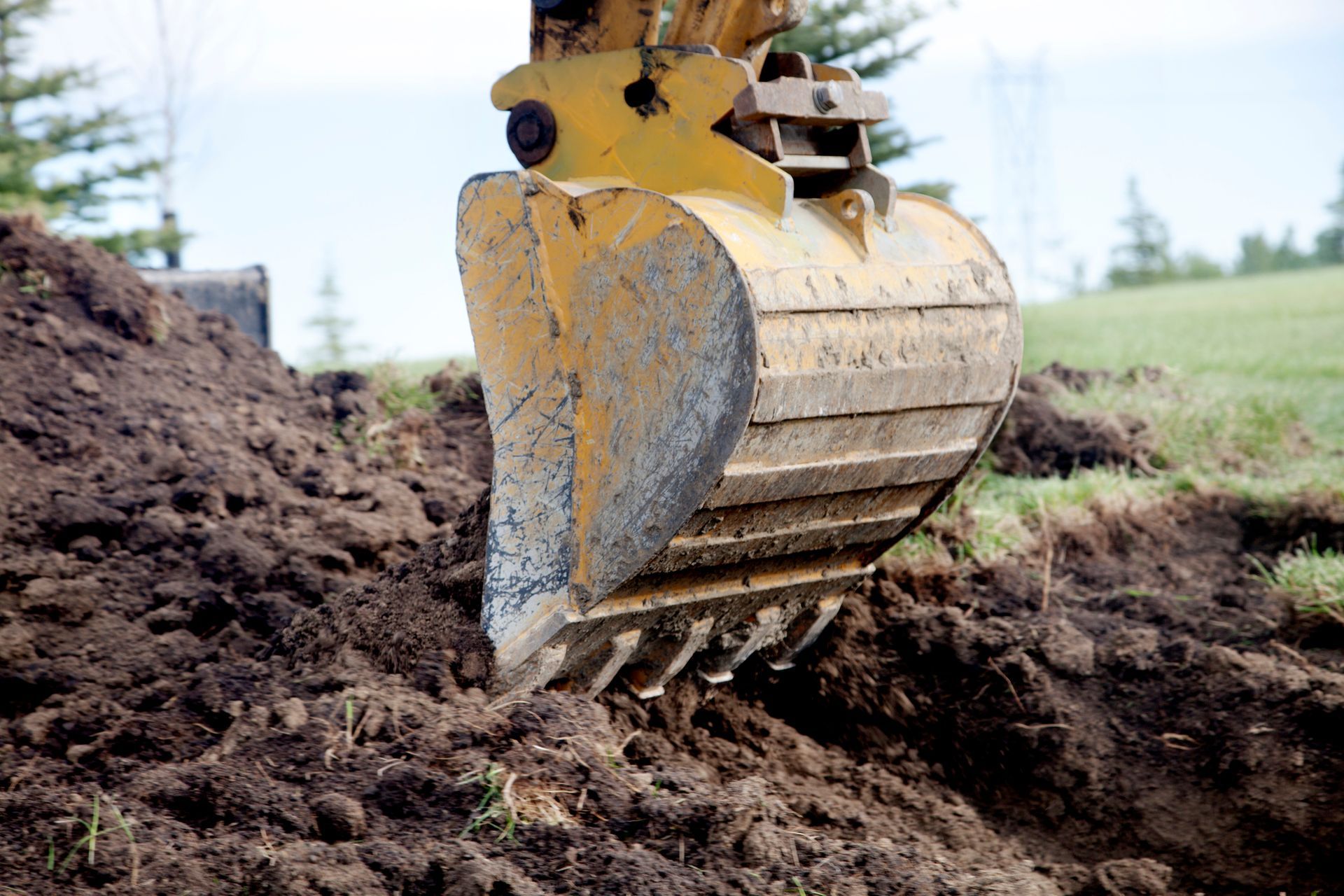 Yellow excavator bucket digging into brown earth.