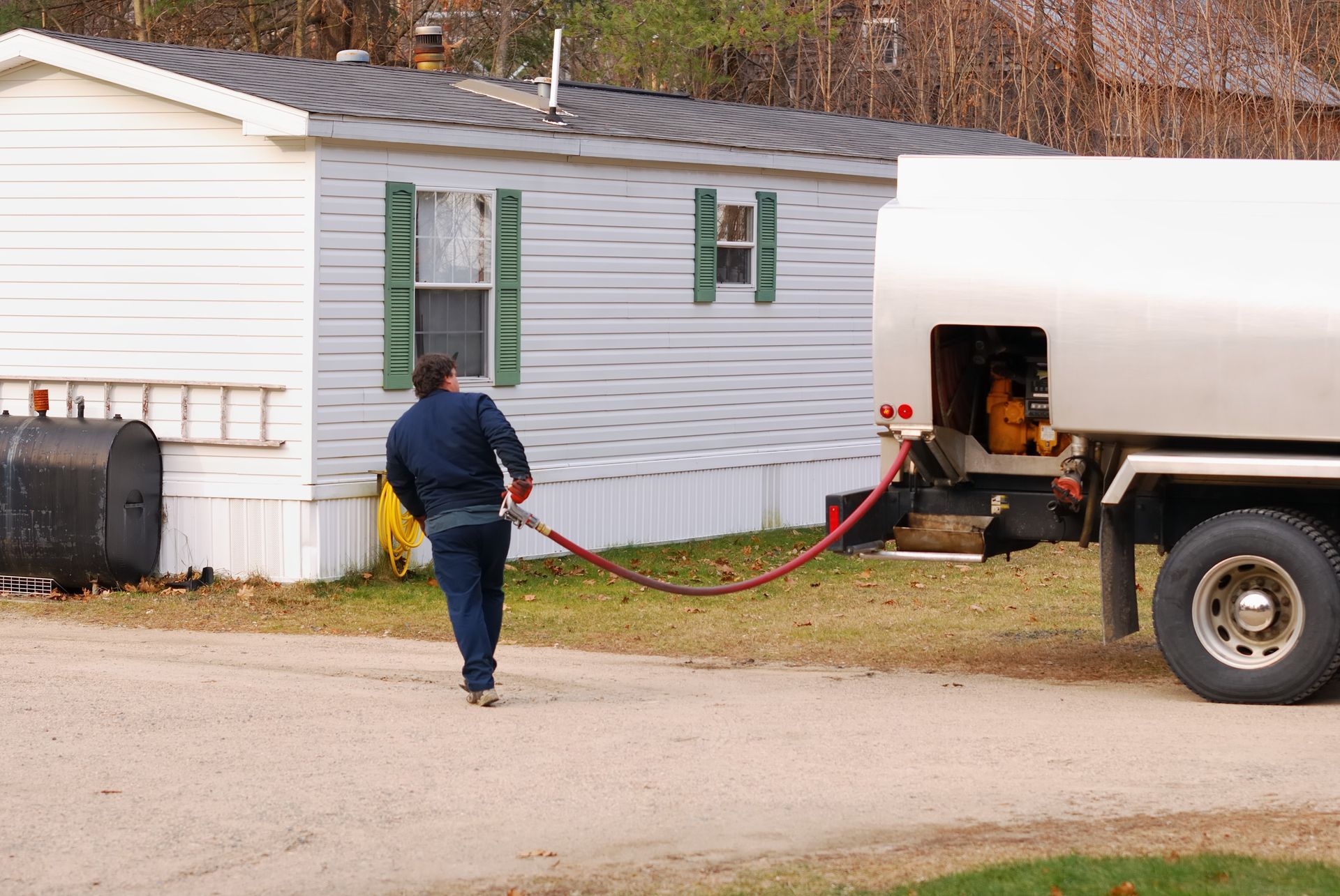 A man is walking towards a tanker truck with a hose attached to it.