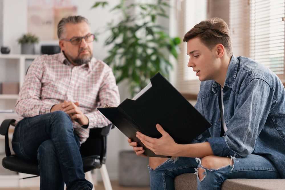Man showing documents to person in a consultation room. Both are focused and seated.