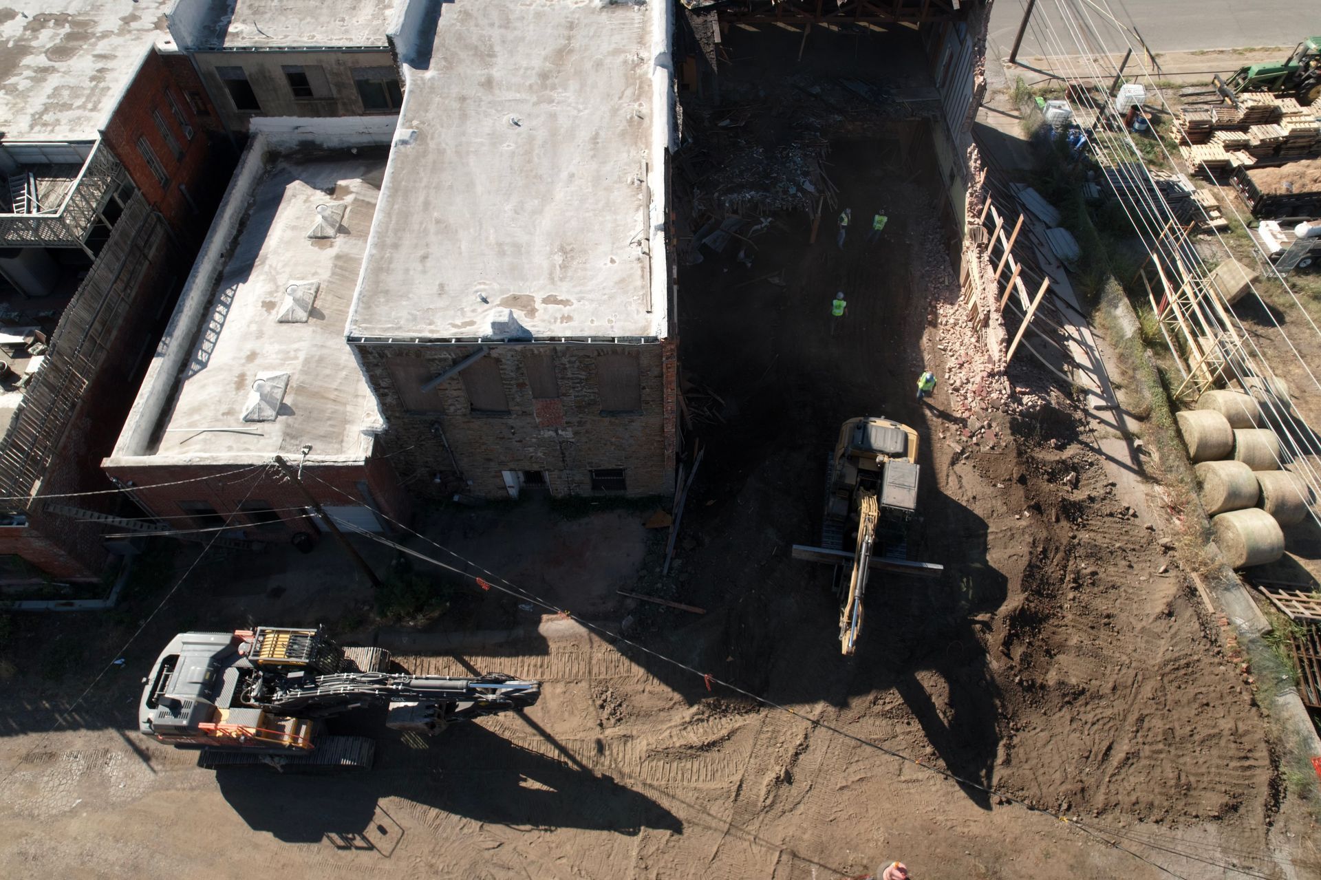 Excavator demolishing a white building against a clear blue sky; debris scattered.