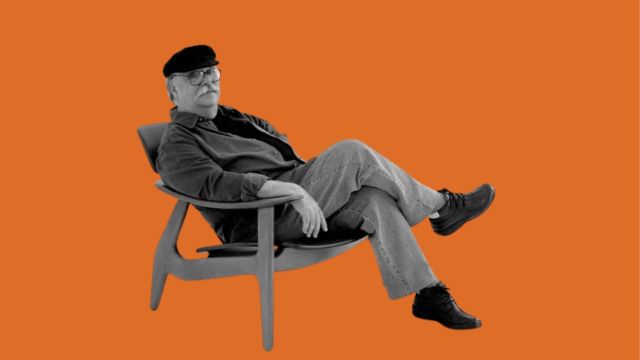 O designer Sérgio Rodrigues sentado confortavelmente em uma de suas criações.