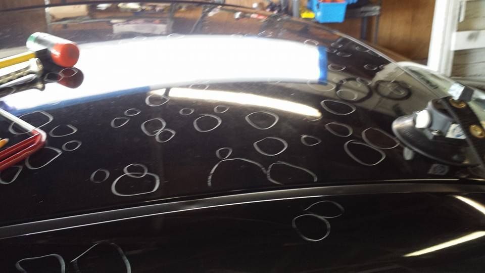 Black car roof with white circles drawn around dents, possibly for repair.