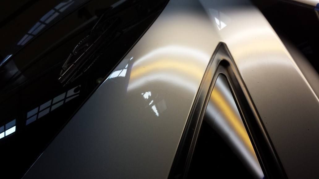 Silver car hood with a dent reflecting light, next to a black trim.