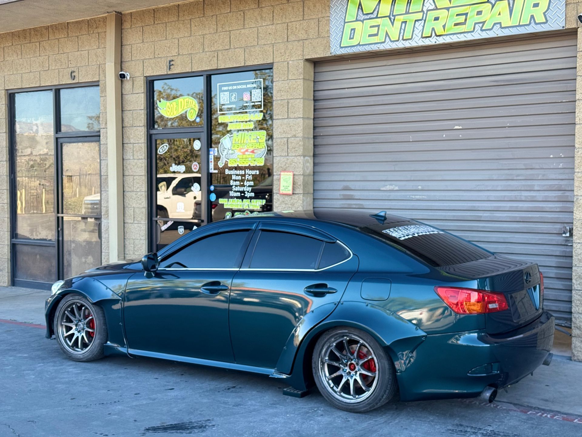 Green Lexus sedan parked in front of a dent repair shop.