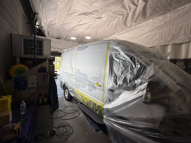 Van covered in plastic and masking tape inside a garage, prepared for painting.