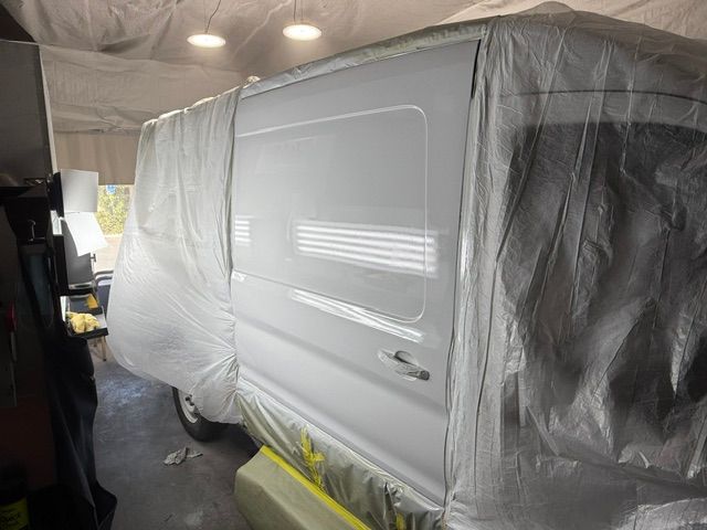 White van being painted in a garage; covered in plastic sheeting.