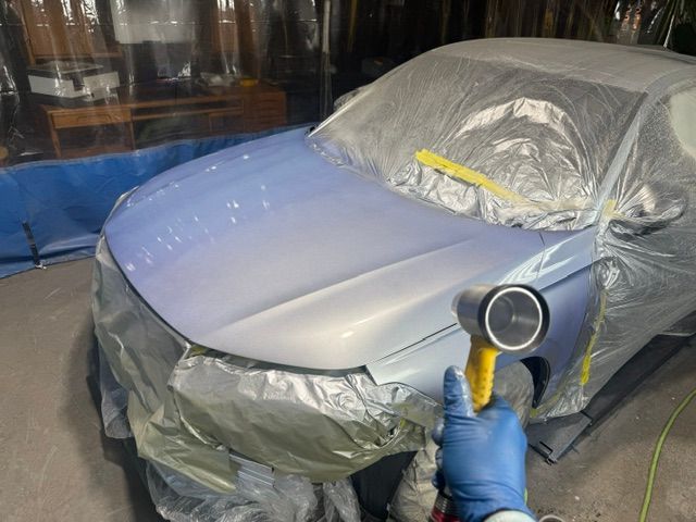 Person in blue glove spraying a light blue car with a paint gun in a paint booth.