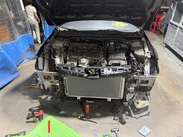 Car with open hood; front end disassembled, revealing radiator and engine components in a repair shop.