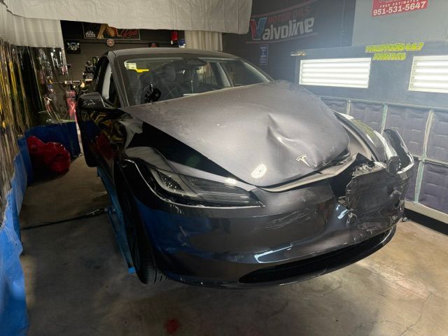 Damaged gray car in a repair shop. Front end heavily dented and crumpled.