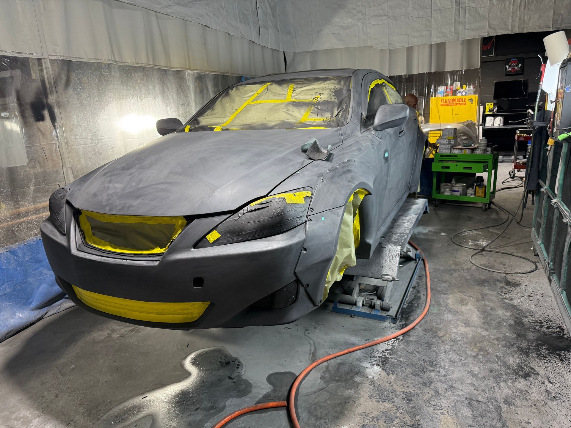Car in a paint booth, covered in primer and yellow tape. Ready for painting.