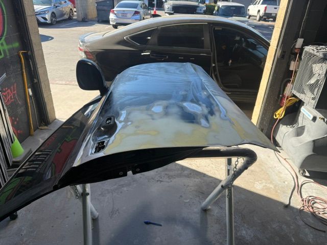 Black car door being prepped for paint in an auto shop. Door is on a stand, showing primer spots.