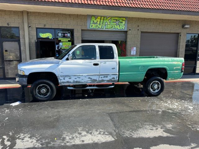 Two-tone Dodge Ram truck parked outside Mike's Dent Repair shop; green bed, silver cab with peeling paint.