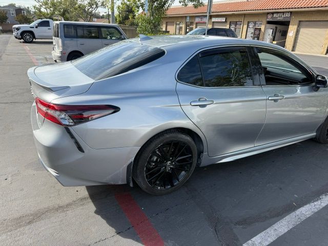 Silver Toyota Camry with black rims parked in a lot, sunny day.
