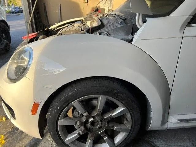 Gray Tesla car parked on a concrete driveway with wheel covers. The car is in front of a house on a sunny day.