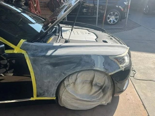 Black SUV being prepped for paint in a garage. Sections are covered in plastic and tape.