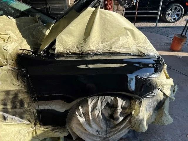 Black SUV, partially covered in plastic, in a garage. Front bumper appears freshly painted.