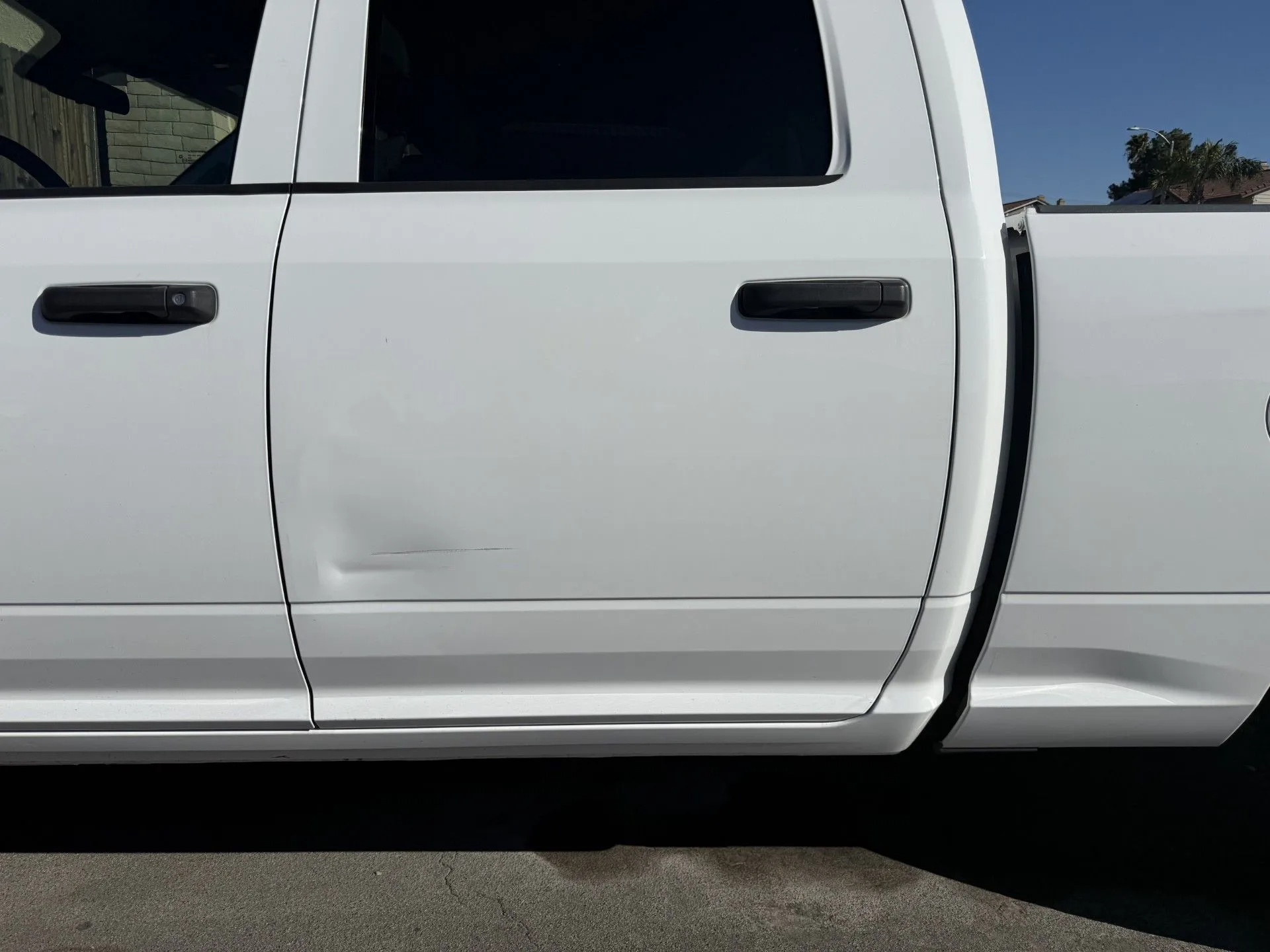 White Ram pickup truck parked on a driveway; a car is visible in the street in the background.