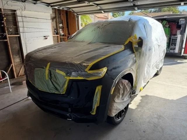 Black SUV being prepped for paint in a garage. Sections are covered in plastic and tape.