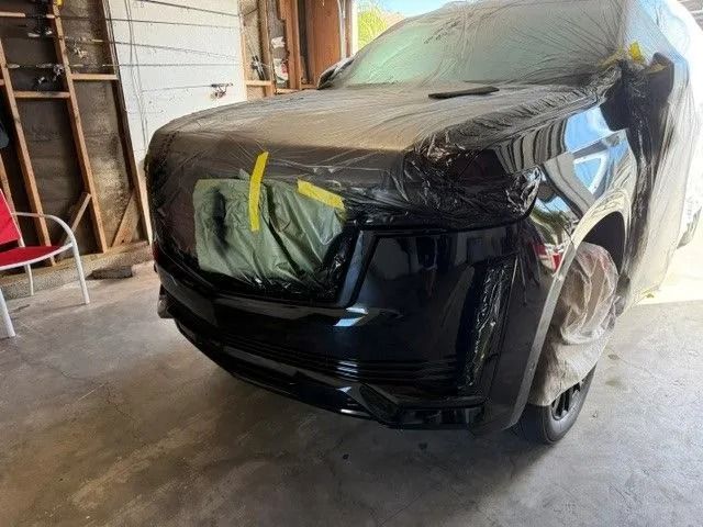 Black SUV, partially covered in plastic, in a garage. Front bumper appears freshly painted.